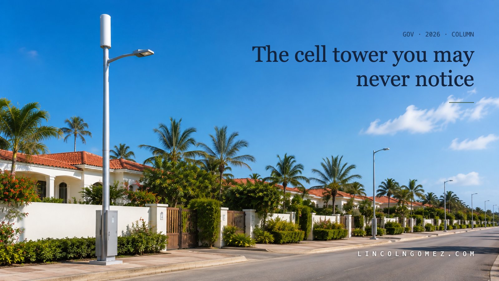 A quiet residential street in Aruba in bright daylight, lined with low white villas, red-tiled roofs and palms. In the foreground a modern streetlight pole doubles as a cellular small cell, with a white cylindrical antenna at the top and a small equipment cabinet at its base, with the article title The Cell Tower You May Never Notice set over the frame at upper left
