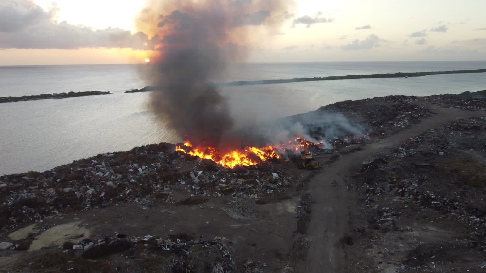 Aerial view of a fire burning along the edge of a coastal landfill at sunset