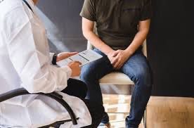 Clinician with a clipboard consulting a male patient seated on an examination couch