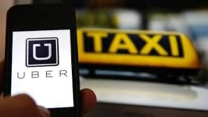 A phone showing the Uber logo held up in front of a yellow taxi roof sign