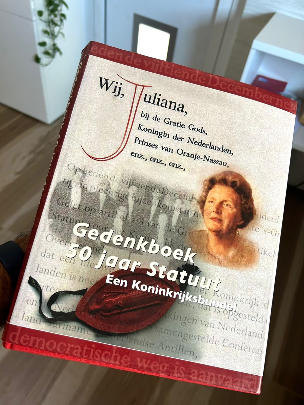 Hand holding a commemorative volume on fifty years of the Charter, with a portrait of Queen Juliana