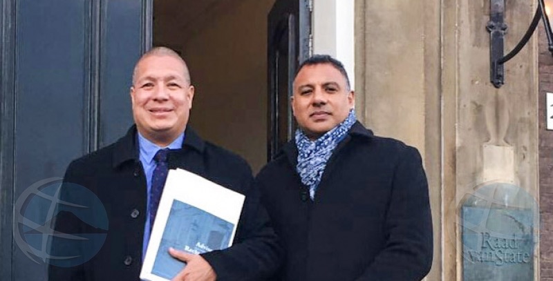 Two men in overcoats outside the Raad van State, one holding a bound advisory report