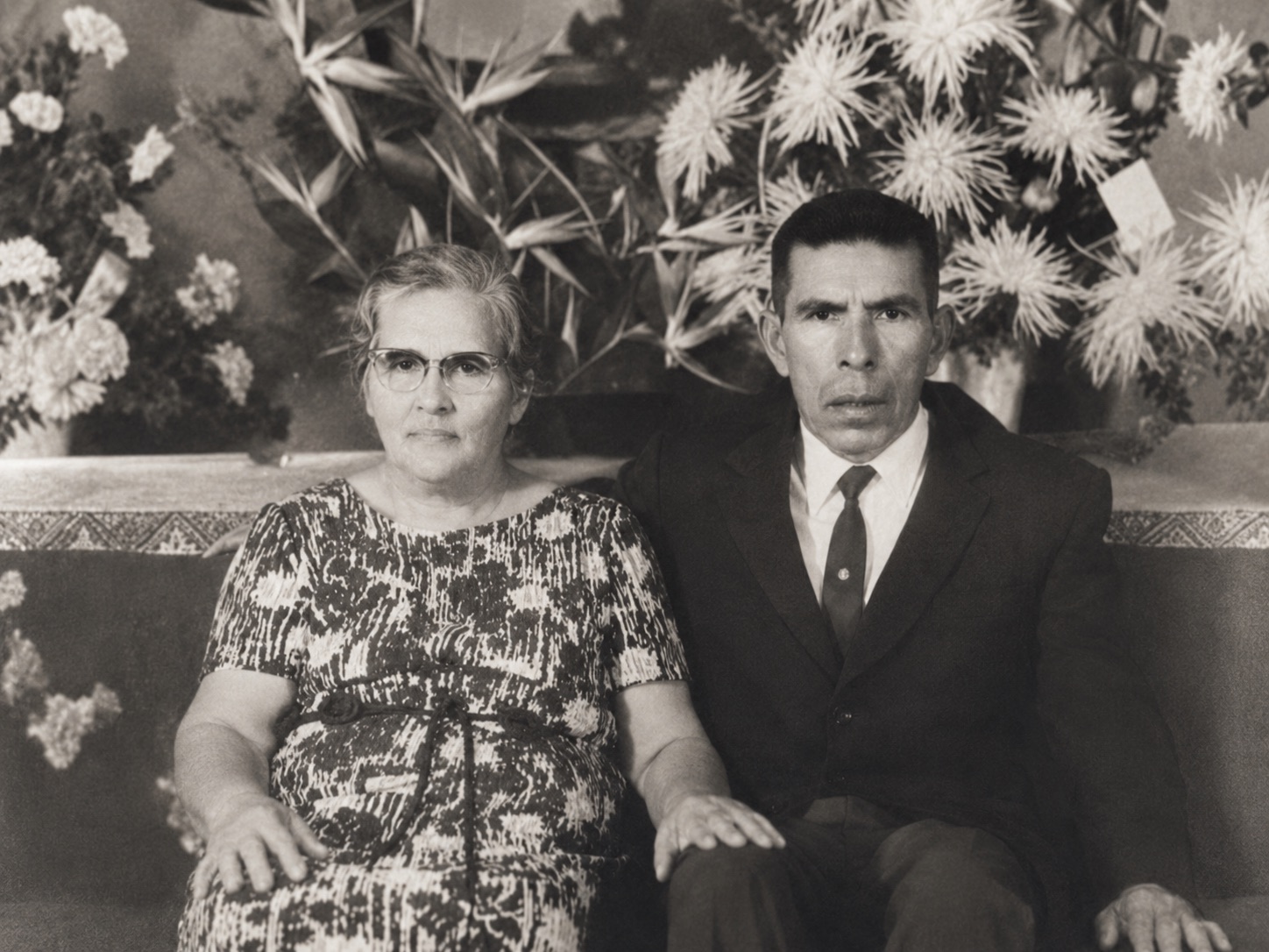 Archival studio portrait of an elderly couple seated before a floral backdrop